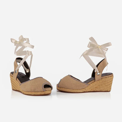 Pair of beige wedge sandals with white ribbons on a white background