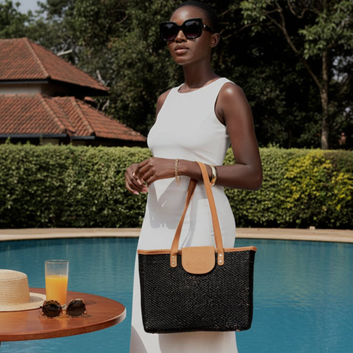 Woman holding a black woven Tote Bag with tan leather accents by a poolside