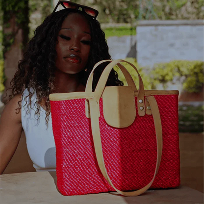Woman holding a red woven tote bag with beige accents outdoors