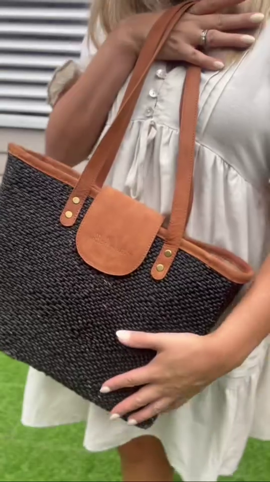 Person holding a black woven tote with brown leather accents