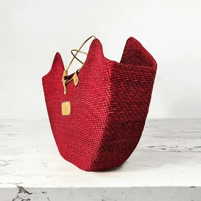 Handcrafted red woven straw beach bag with brass handles and a tan leather tag.