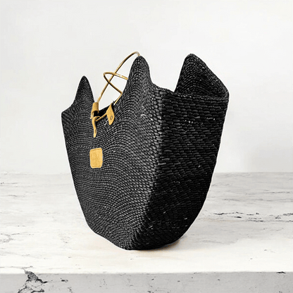 Handcrafted black woven seagrass beach bag with brass handles and a tan leather accent.