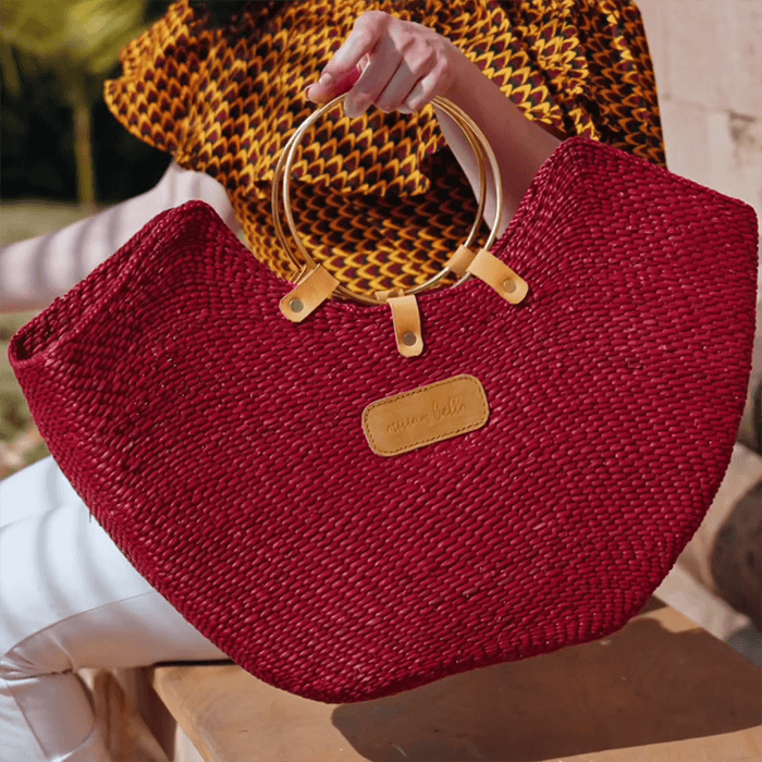Handcrafted Jua woven straw beach bag in deep red with elegant brass ring handles and a leather label.
