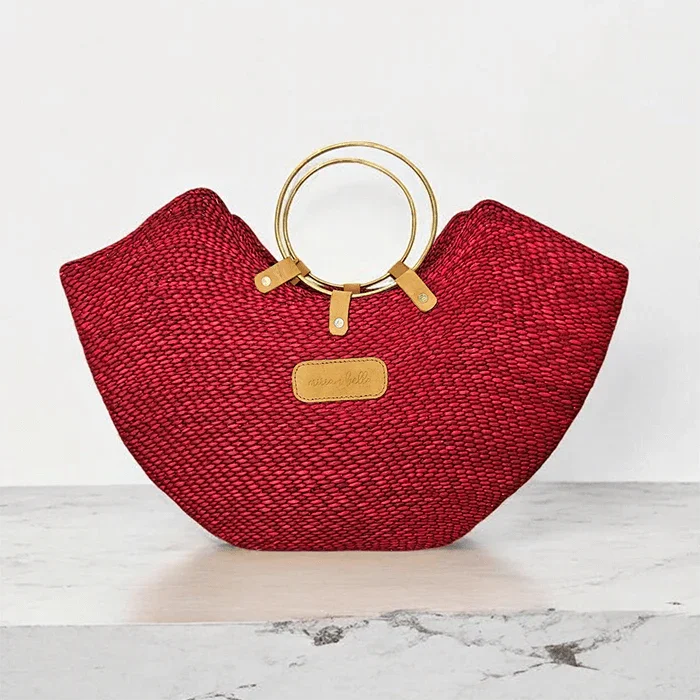 Red woven straw beach bag with elegant brass ring handles and a leather label.