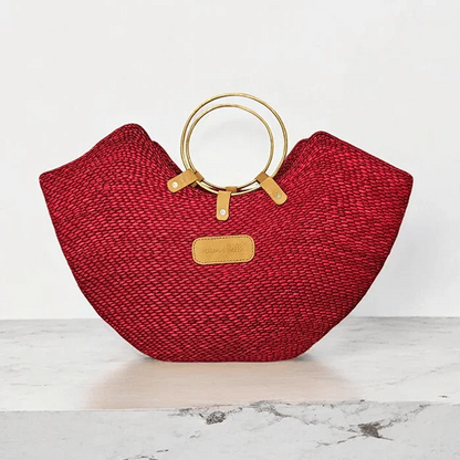 Red woven straw beach bag with elegant brass ring handles and a leather label.