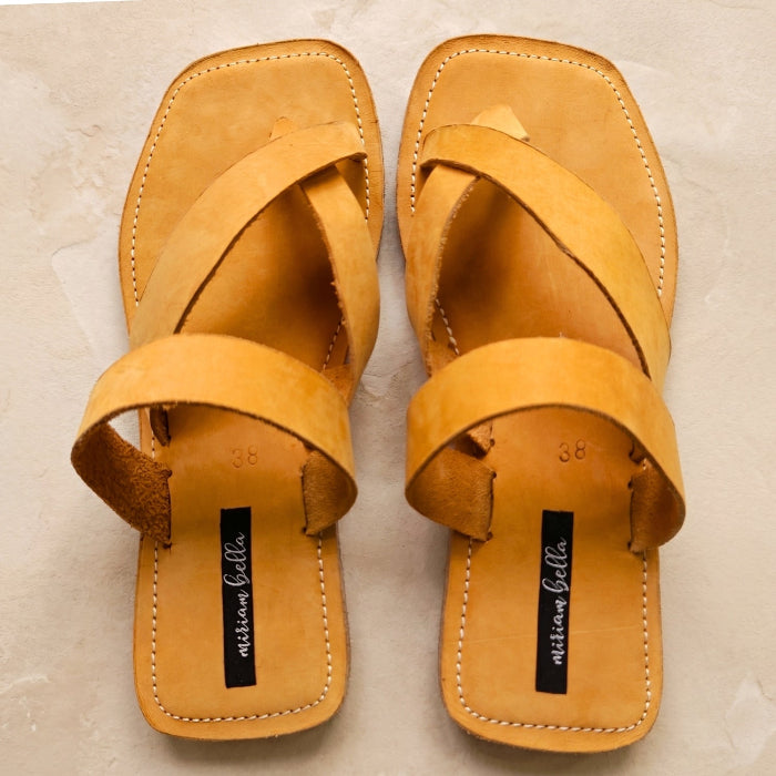 Image of handmade tan leather sandals with cross strap produced by Australian brand Miriam Bella on a light beige background