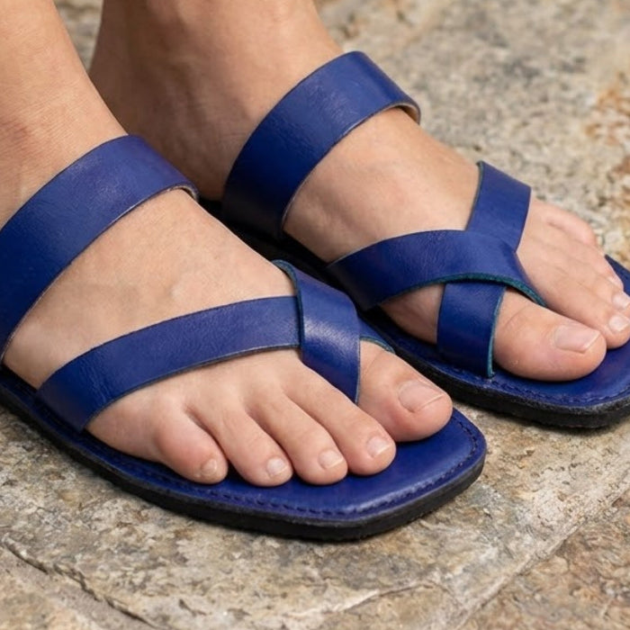 Handmade indigo leather sandals with cross strap produced by Australian brand Miriam Bella worn on feet standing on a stone surface