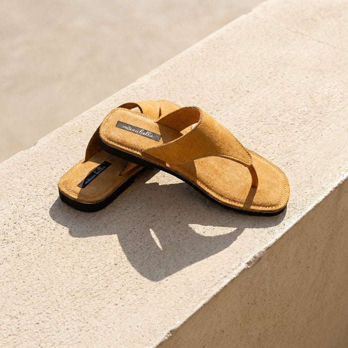 A  pair of women's leather slides with wedge heel, produced by Australian brand Miriam Bella on a light surface with water in the background