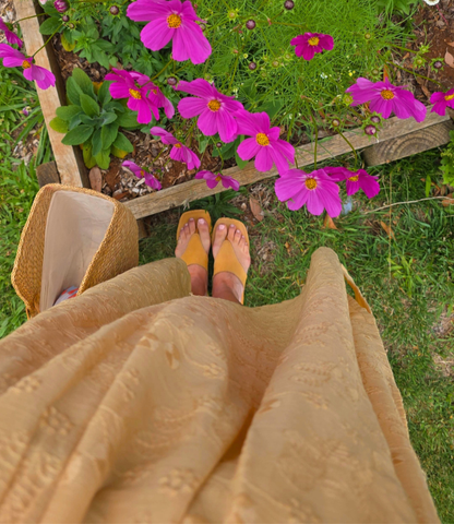 Person wearing a beige dress and tan Women's leather slide sandals standing on grass with pink flowers in the background.