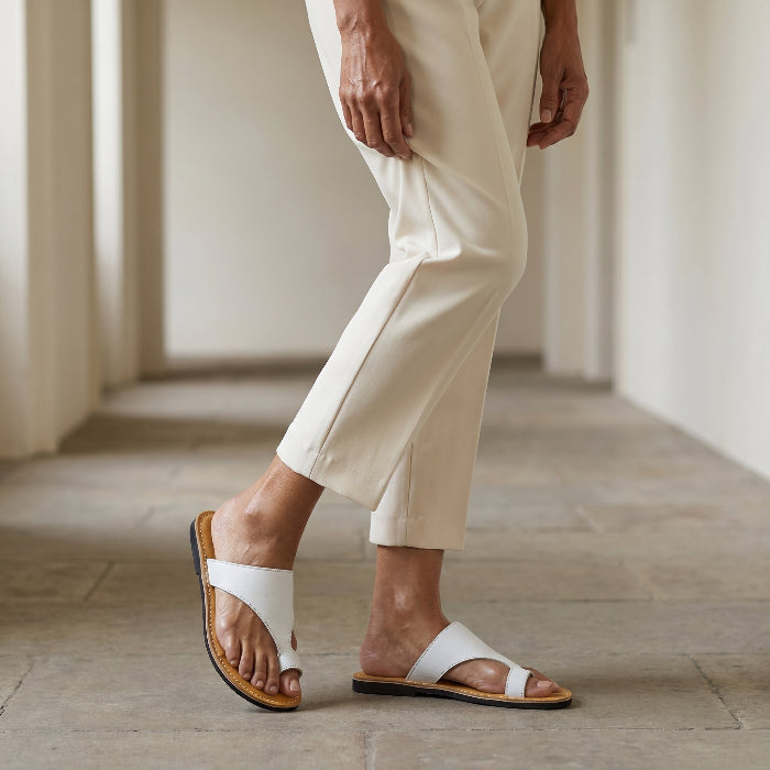 Person wearing white thong sandals by Miriam Bella on a neutral background