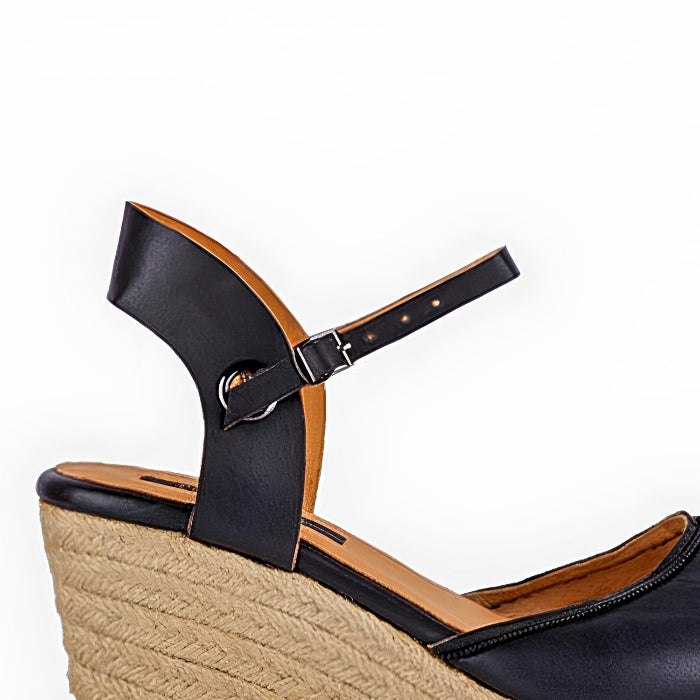 A close up of a handcrafted leather black wedge espadrille sandals with jute sole by Miriam Bella on a white background.