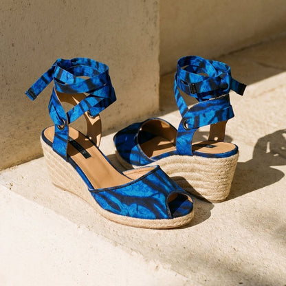 Gaia Ocean Spirit espadrille wedge sandals with blue ankle ties on a light stone surface.