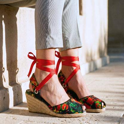 Gaia Wild Flame espadrille wedge heels with red ribbon ankle ties and printed canvas worn by a person on a stone pavement.