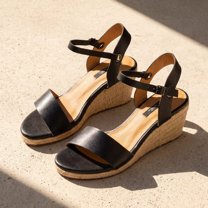 A pair of Gaia blasck leather open toe espadrille wedge sandals on a stone terrace