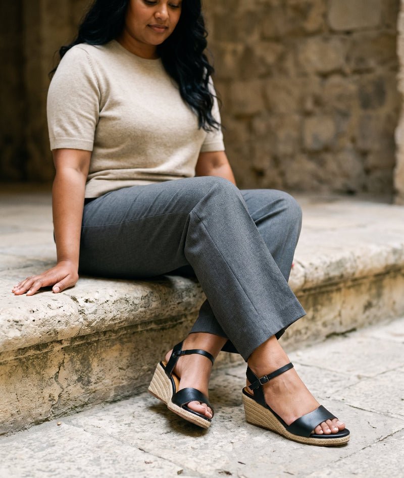 Woman wearing Gaia black leather open toe espadrille wedge sandals with gray trousers and a cream knit top.