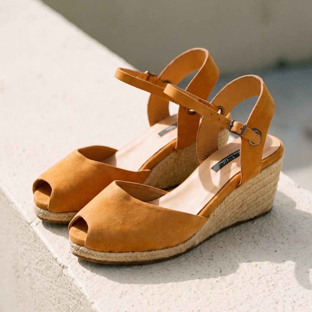 A pair of tan leather wedge sandals with espadrille-style jute-wrapped wedge heels and adjustable ankle straps, photographed on a light concrete surface in bright natural light.
