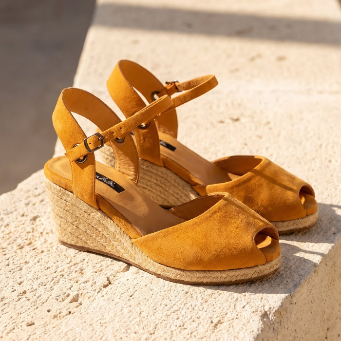 A pair of handcrafted leather ochre wedge espadrille sandals with jute sole by Miriam Bella on a stone bench