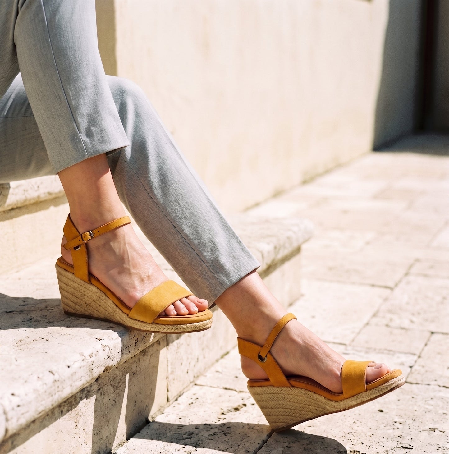 Woman wearing Gaia ochre leather open toe espadrille wedge sandals with grey pants standing on a stone terrace