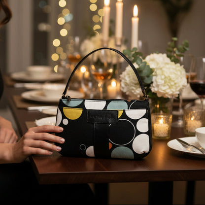 Woman holding the Black Print Mini Tote Bag for Wome,  a patterned handbag at a dinner table with candles and flowers.