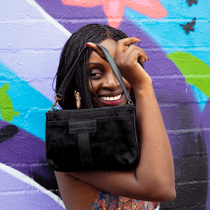 Woman holding a Black Mini Bag in front of a colorful mural