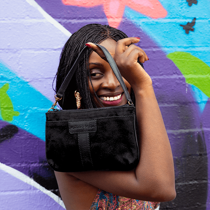 Woman holding a Black Mini Bag in front of a colorful mural