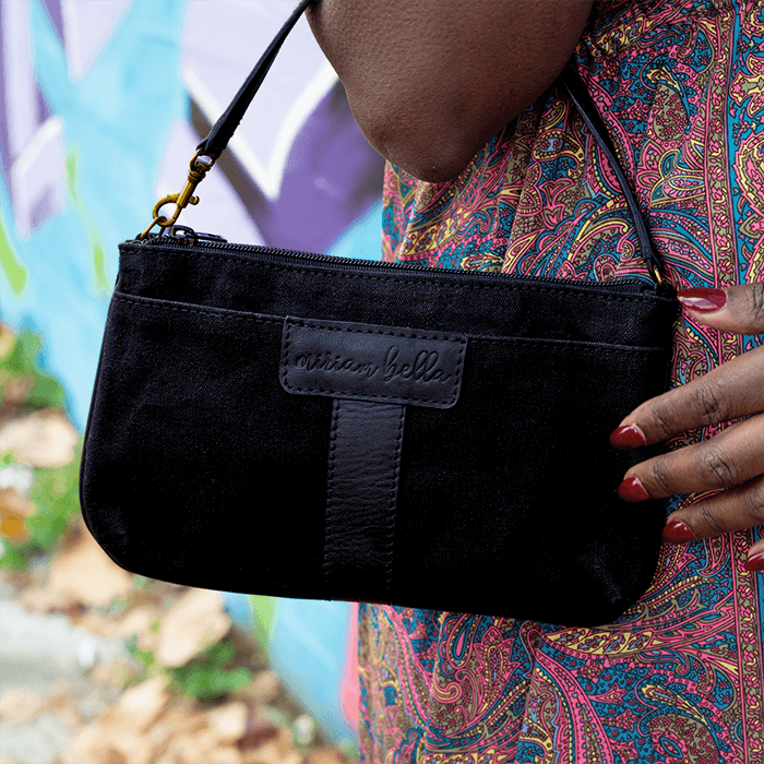 Black Mini bag held by a person with a colorful patterned garment, blurred natural background