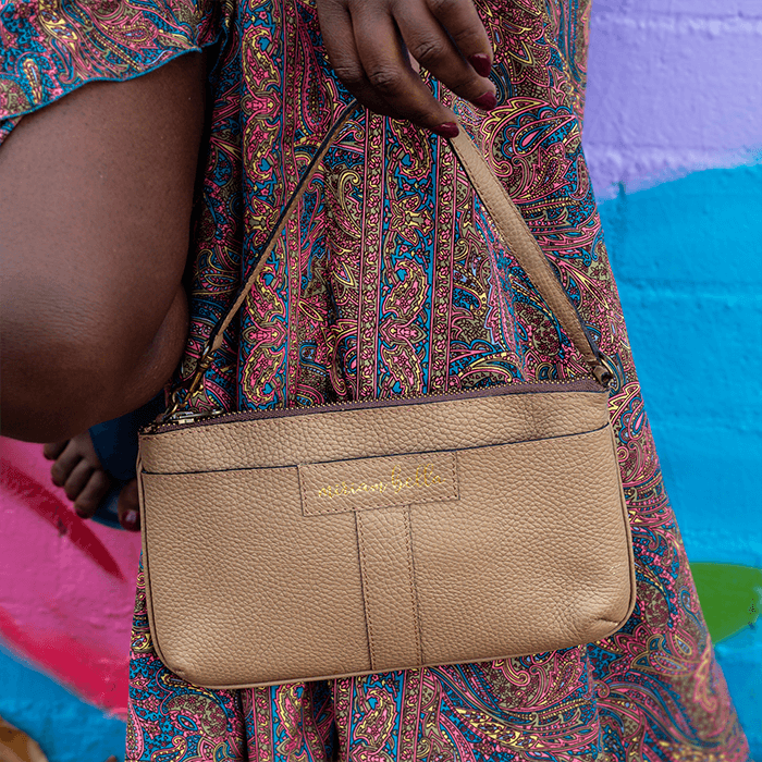 The Mini Tote, a beige handbag held by a person wearing a colorful patterned dress against a multicolored background.