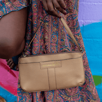 The Mini Tote, a beige handbag held by a person wearing a colorful patterned dress against a multicolored background.