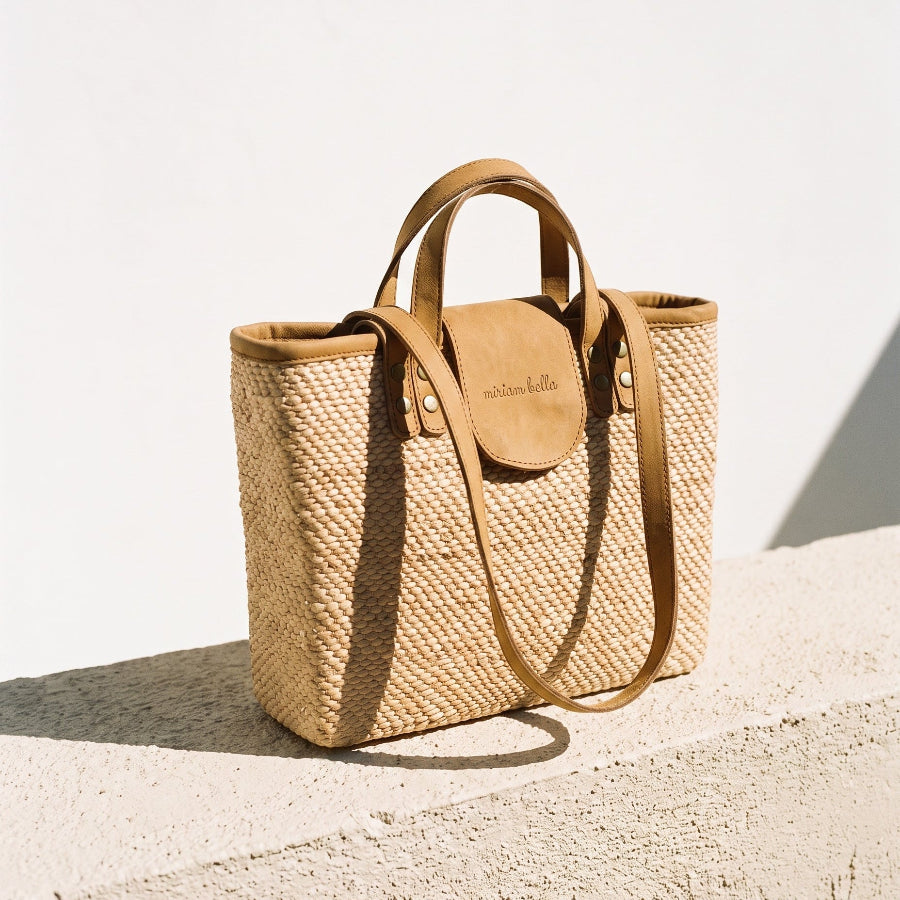 Woven tote bag with leather handles on a stone bench.