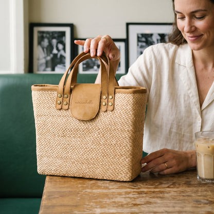 A woman holding a Woven tote bag with leather handles on a wooden cafe table 