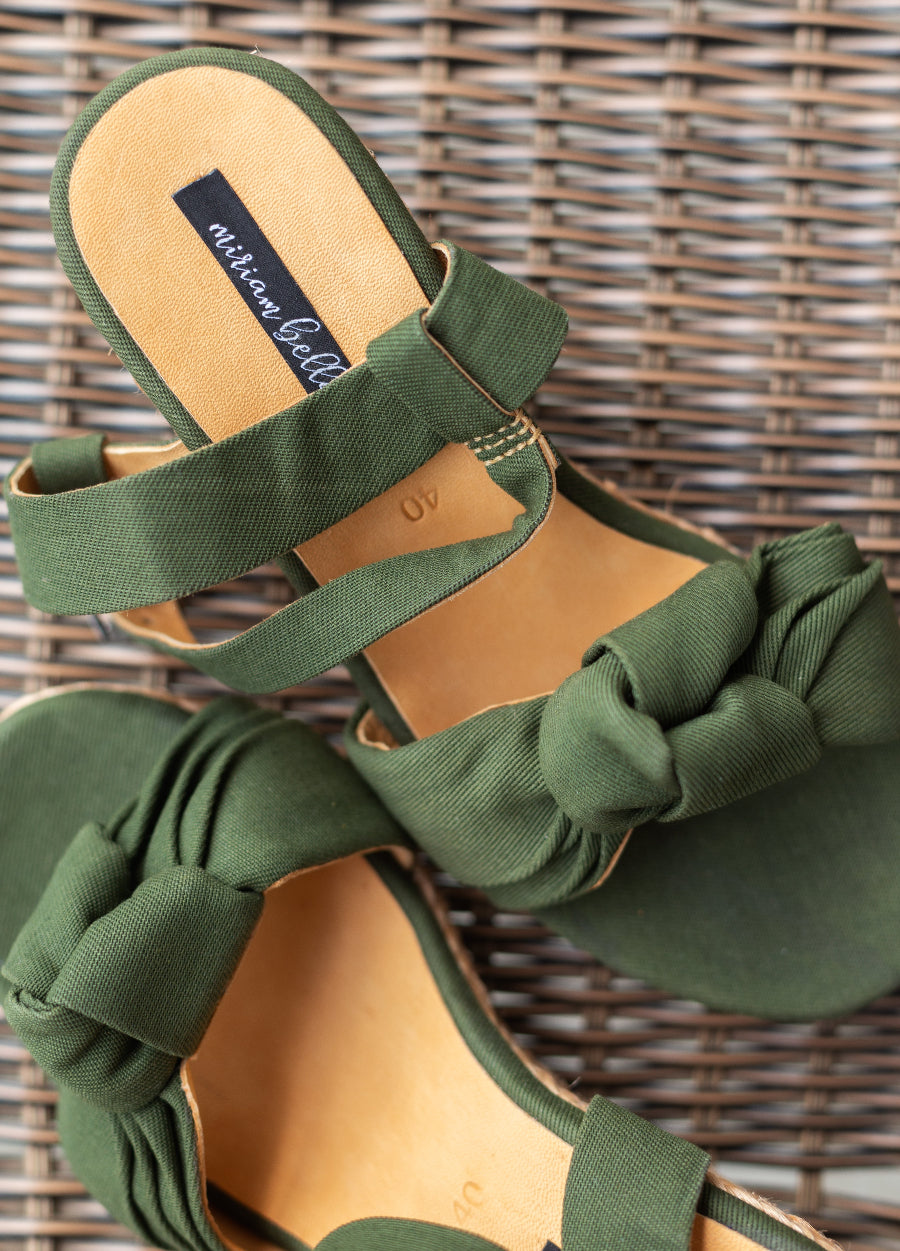A pair of women's strappy flat sandals in olive green fabric with knotted bow details on the toe, shown on a woven wicker background. The insoles are tan with a visible 'michael lafferty' brand label.