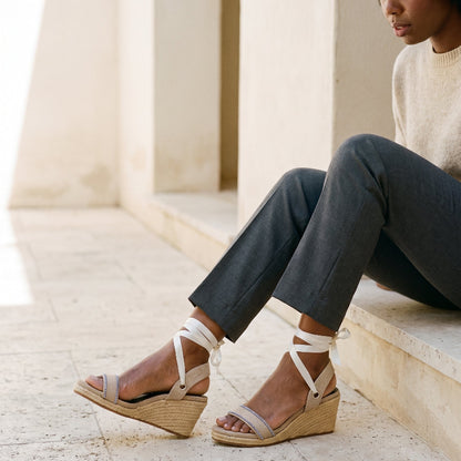 A woman wearing Gaia cream canvas wedge espadrilles with cream ankle ties sitting on stone steps.