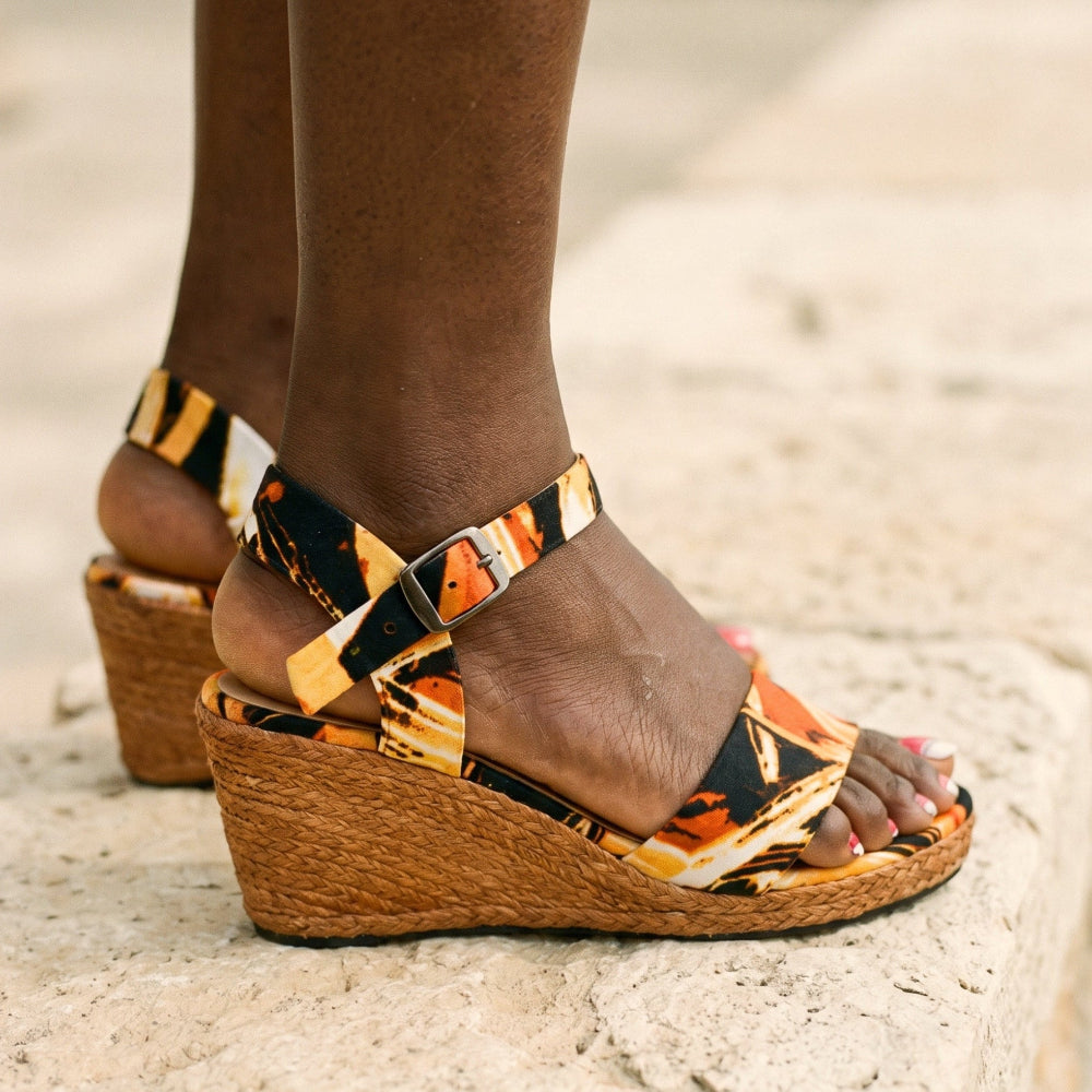 A close-up of a person wearing patterned wedge sandals with woven espadrille-style heels, standing on a stone surface outdoors.