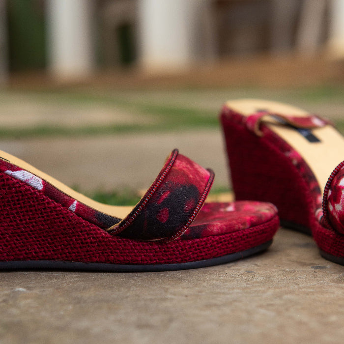 Red women's espadrille wedge sandals on a stone surface with a blurred outdoor background