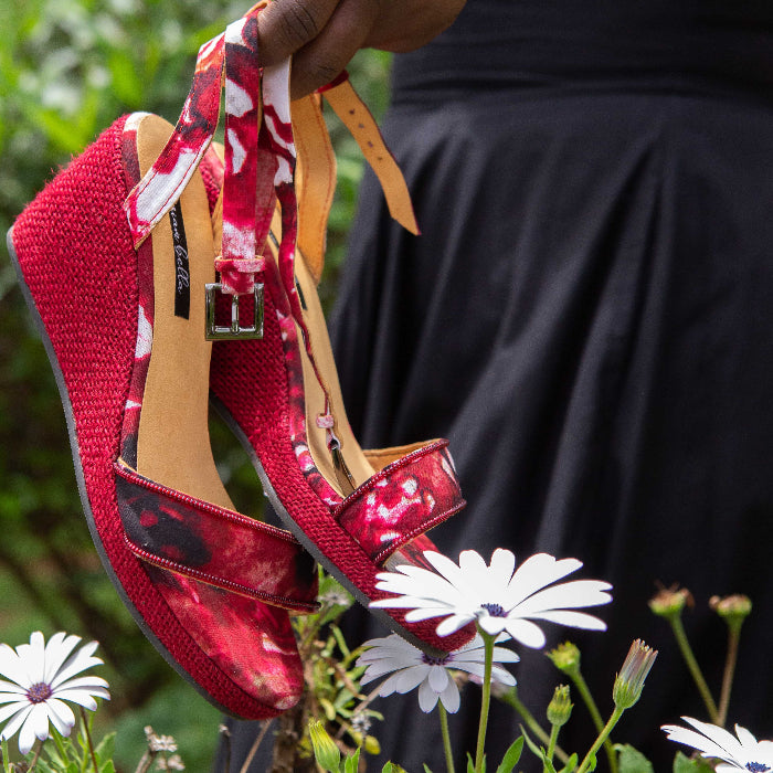 Red women’s espadrille wedge sandals with floral pattern held above flowers