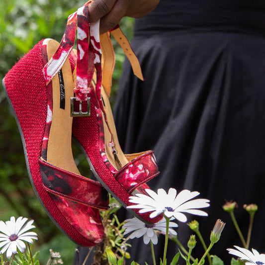 Red women’s espadrille wedge sandals with floral pattern held above flowers