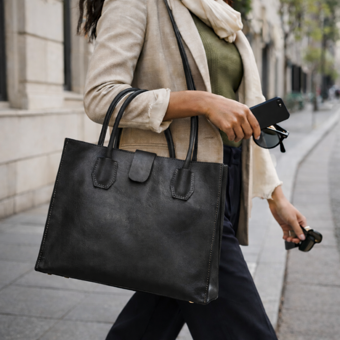 Person holding a black leather tote handbag on a city street
