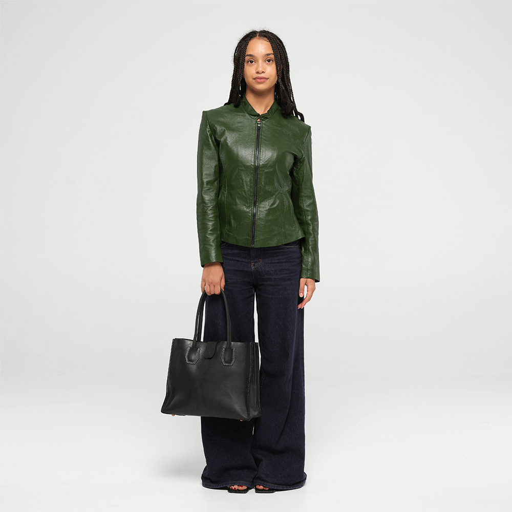 Woman wearing a green leather jacket holding a black leather tote handbag on a white background