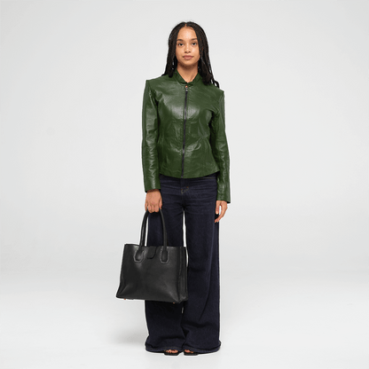 Woman wearing a green leather jacket holding a black leather tote handbag on a white background