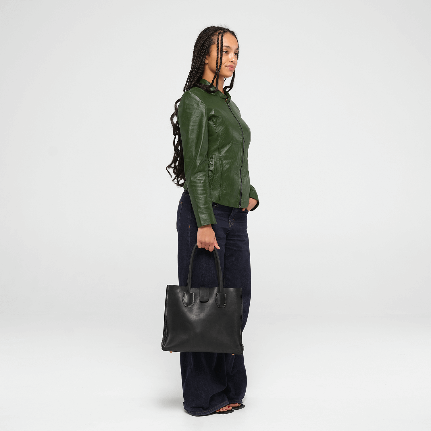 Person wearing a green leather jacket and holding a black leather tote bag on a white background