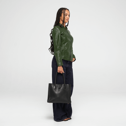 Person wearing a green leather jacket and holding a black leather tote bag on a white background