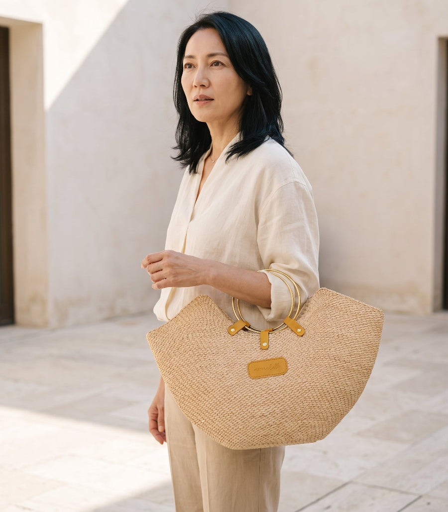 A woman holding Jua woven straw beach bag with brass ring handles in natural colour.