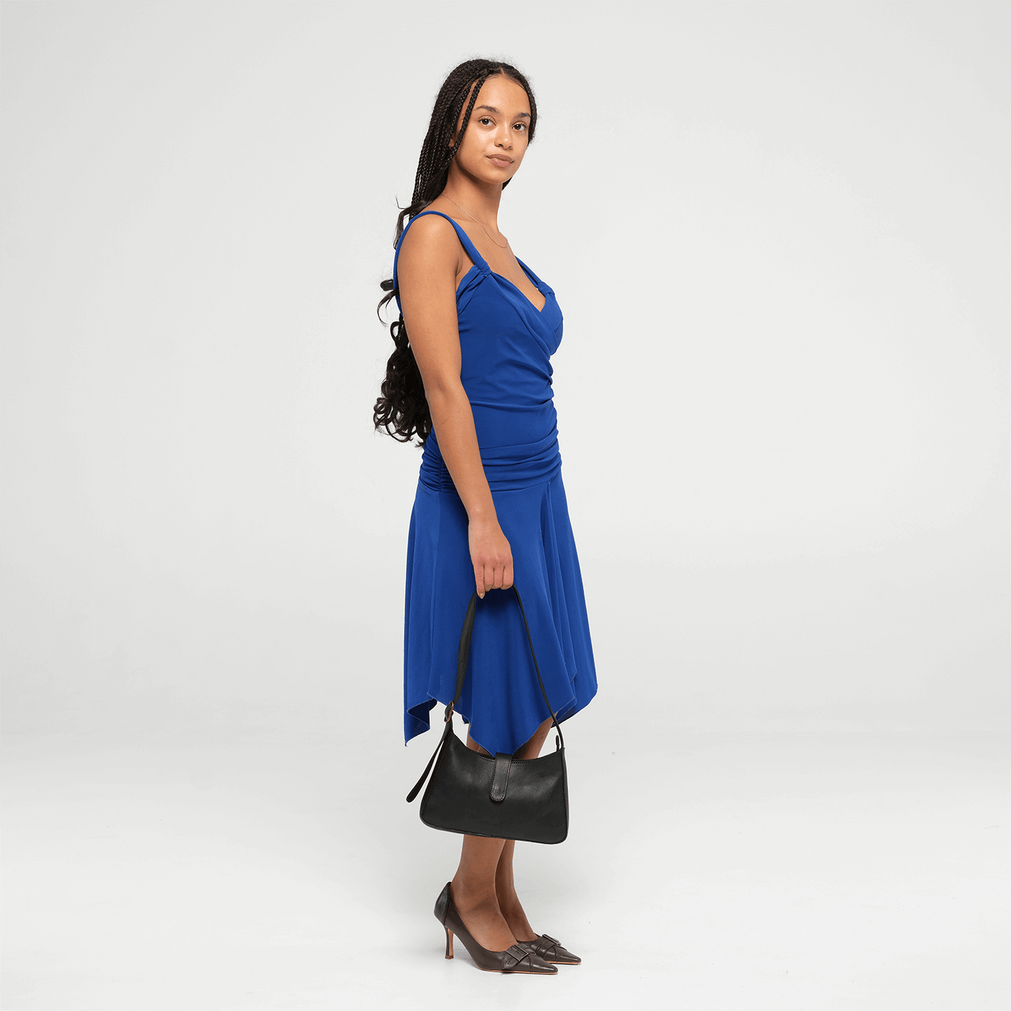Woman wearing a blue dress holding a small black shoulder bag on a white background