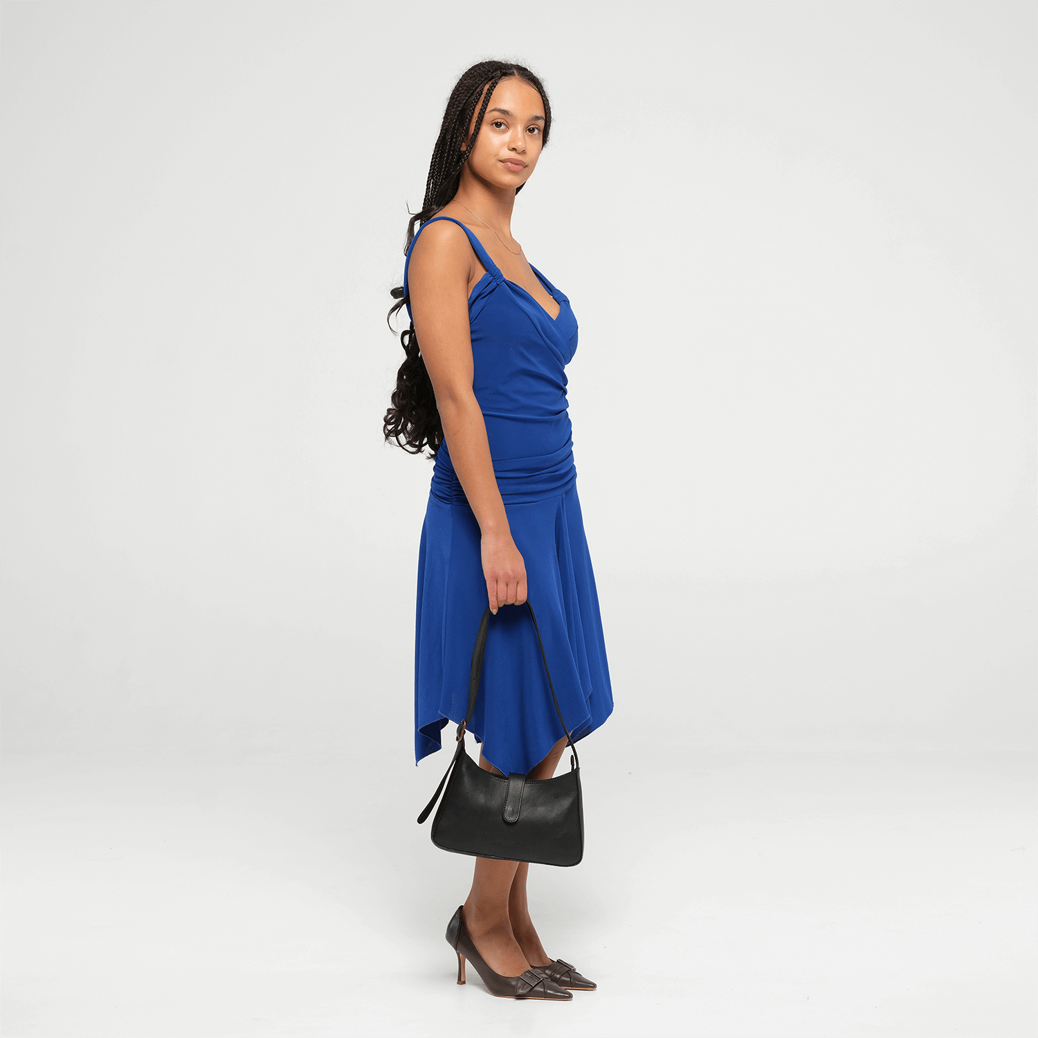 Woman wearing a blue dress holding a small black shoulder bag on a white background
