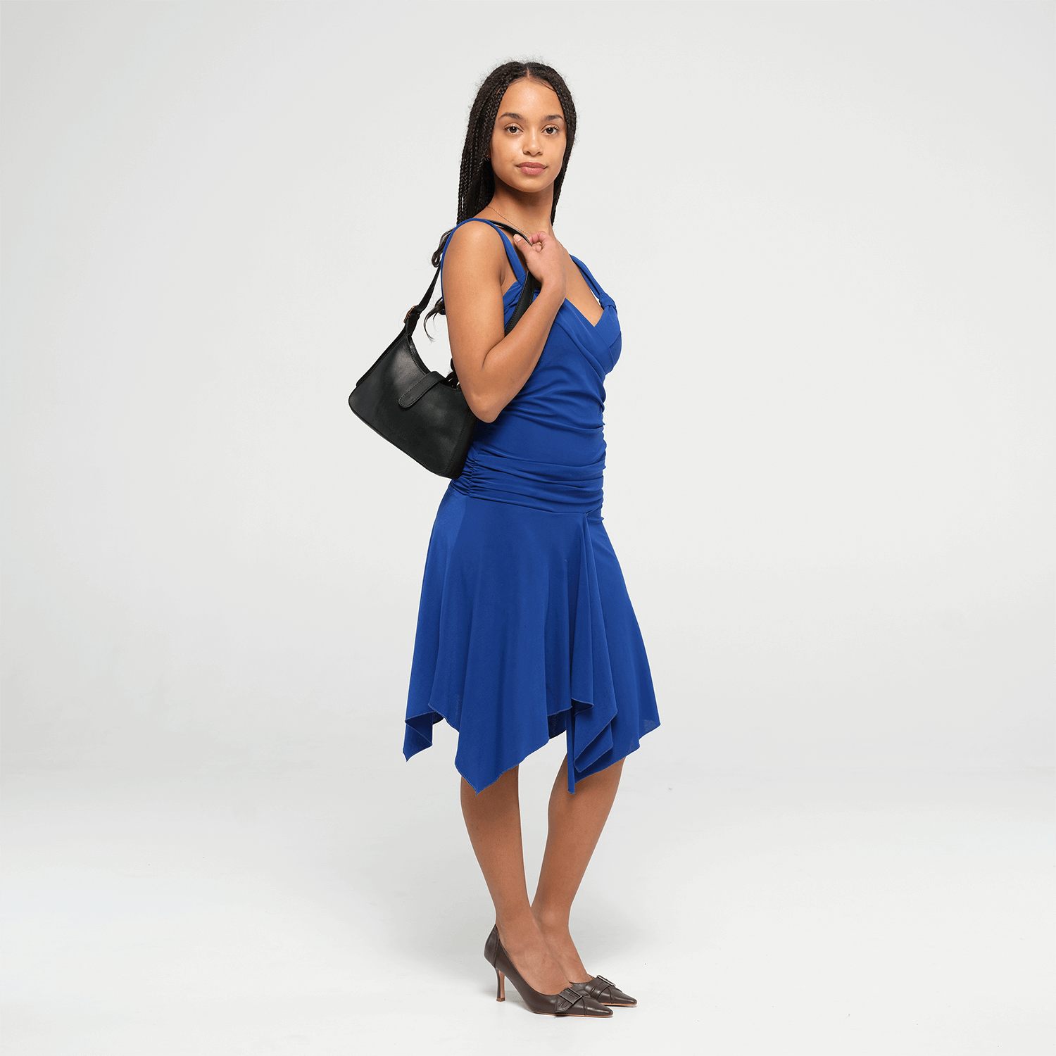 Woman wearing a blue dress with a black leather mini shoulder bag on a white background