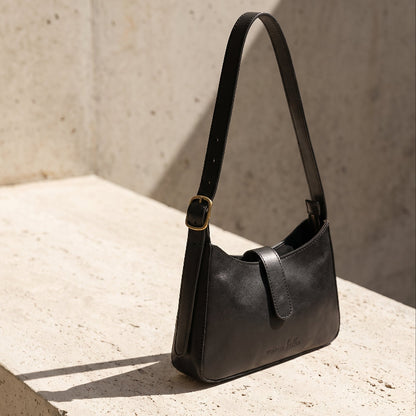 Black leather mini shoulder bag on a concrete surface with a neutral background