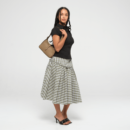 Woman holding an olive leather mini shoulder bag with a strap on a white background wearing a black top and plaid skirt on a white background
