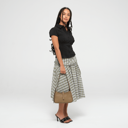 Woman wearing a black top and plaid skirt with an oIive leather mini shoulder bag  on a white background