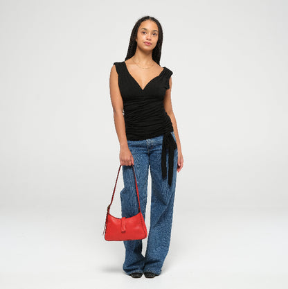 Woman wearing a black top and blue jeans, holding a red leather mini shoulder bag on a white background