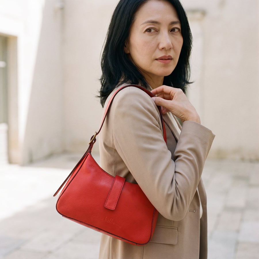 Woman holding a red leather mini handbag against a blurred background